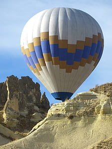 white, brown, and blue hot air balloon on mid air beside brown mountains at during daytime thumbnail