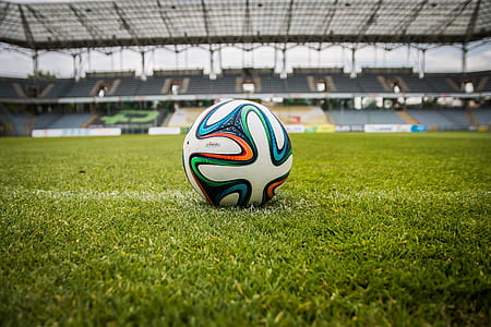 white, orange, and green soccer ball on green grass field thumbnail