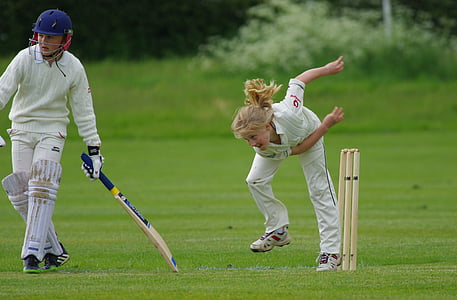 girl standing beside cricket stumps near boy holding cricket bat thumbnail