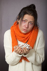 woman wearing sweater and scarf holding medication tablets thumbnail