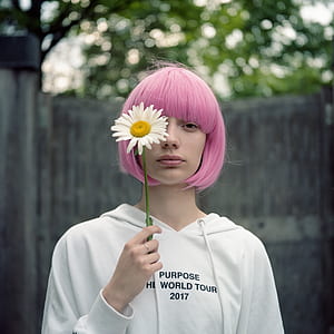 woman holding white daisy flower covering her right eye during daytime thumbnail