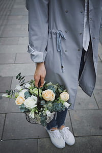 person wearing gray long coat holding basket of white and peach roses thumbnail