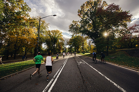 group of people running on street surrounded by green leaf trees thumbnail