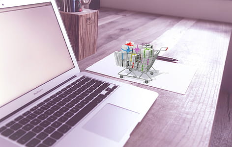 Photo illustration of online shopping and ecommerce. Open laptop computer with shopping cart full of presents, wrapped. thumbnail