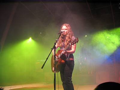 woman playing guitar while singing on stage thumbnail