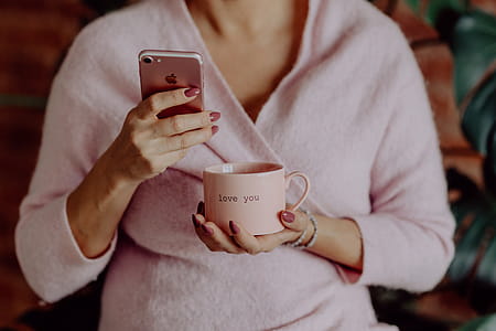 A woman in a pink sweater holds a pink iPhone and a pink cup in her hands thumbnail