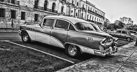 Greyscale Photo of Vintage Car Parked Beside Building thumbnail