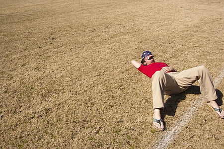 man wearing red t-shirt and brown pants lying on brown grass field thumbnail