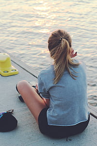 woman in gray top sitting on dock near body of water thumbnail