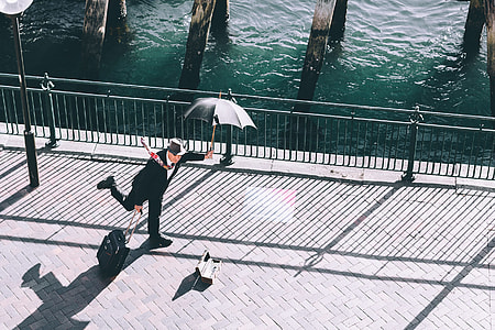man in black 2-piece suit holding black parasol and trolley luggage thumbnail