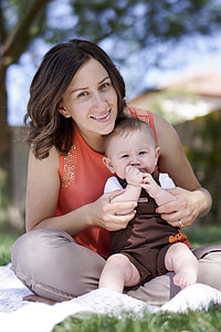 boy wearing brown overall shorts sitting on woman wearing orange sleeveless top and gray pants thumbnail