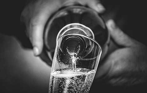 grayscale photo of person holding bottle filling clear glass thumbnail