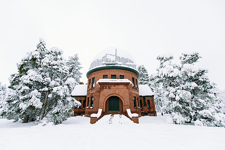 brown concrete house covered with snow near pine trees thumbnail
