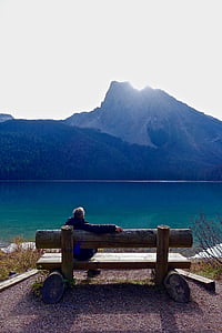 man sitting on brown wooden bench in front of lake during daytime thumbnail