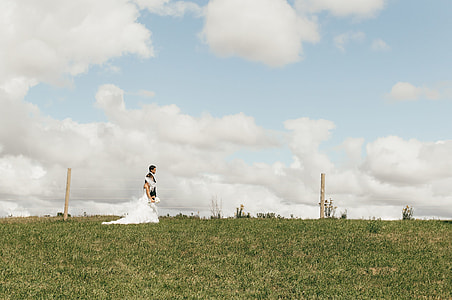 newlywed couple walking on field under white and blue sky thumbnail