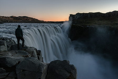 man standing near waterfall under white sky at daytime thumbnail