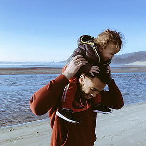 man carries toddler on back of his head at the beach thumbnail