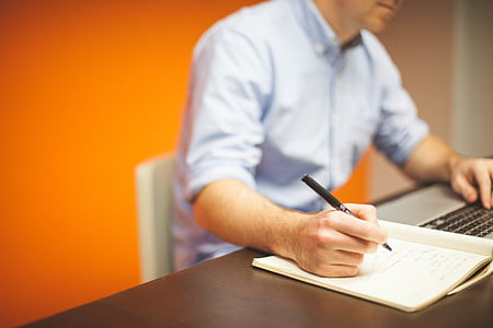 man writing and using laptop beside table thumbnail
