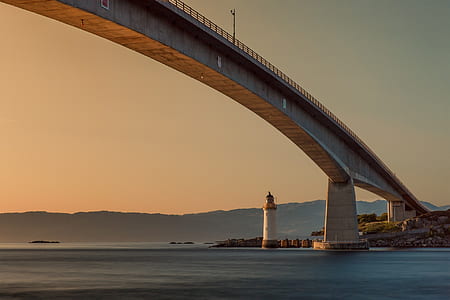 lighthouse under gray bridge during golden hour thumbnail