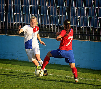 two woman playing soccer beside blue wall thumbnail