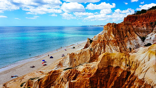 rock formation mountain beside ocean under white clouds and blue sky thumbnail