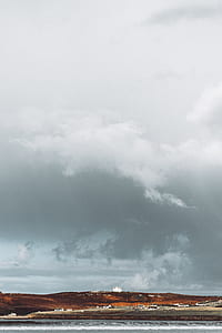 buildings on brown hill near body of water under gray cloudy sky at daytime thumbnail