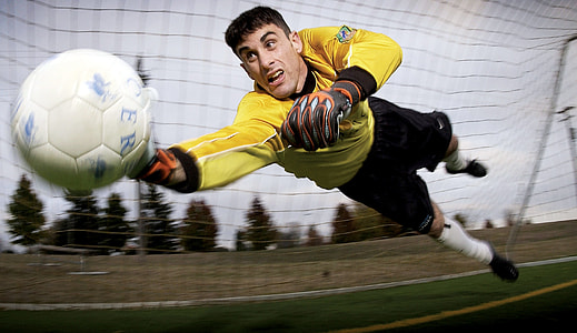 man wearing yellow long-sleeved shirt and black shorts with white socks and black shoes catching a football ball thumbnail