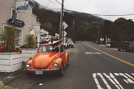 orange Volkswagen Beetle coupe on road near brown building thumbnail