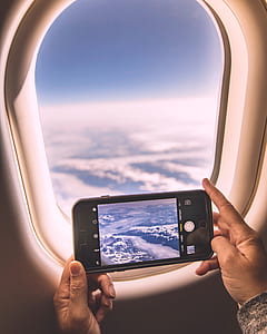 person in airplane using iPhone capturing clouds during daytime thumbnail