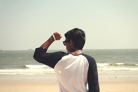 Man in White and Black Raglan Shirt Standing in the Seashore at Daytime thumbnail