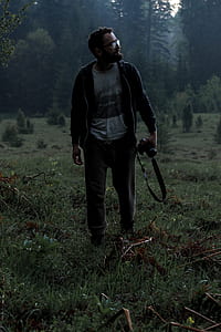 man in black jacket standing holding camera on grass field thumbnail