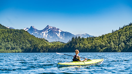 woman kayaking on body of water beside forest and mountains thumbnail