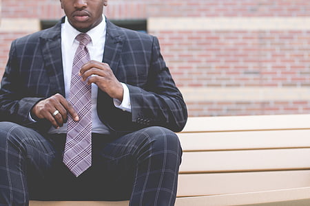 man wearing black-and-gray formal suit sitting on brown wodoen bench thumbnail