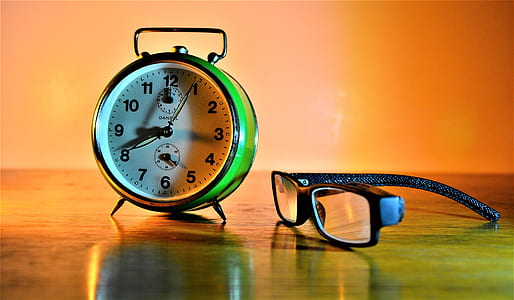 green bell alarm clock beside eyeglasses with black frames thumbnail