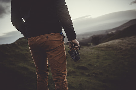 person standing on mountain slope holding camera thumbnail