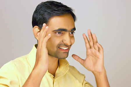 man raising hand while smiling near wall thumbnail