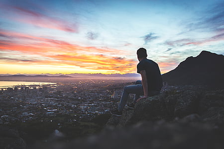 man sitting on rock formation during sunset thumbnail