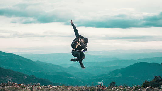 man wearing black shirt jumping while doing dab during daytime thumbnail