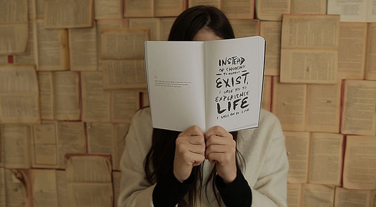 woman holding a book with Instead Exist Life text near wall thumbnail