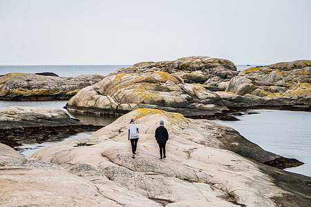 two men waling on rock near body of water thumbnail