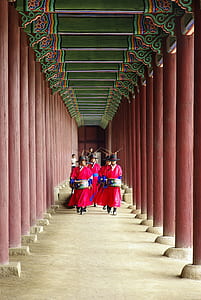 people walking while carrying drums between pillars thumbnail