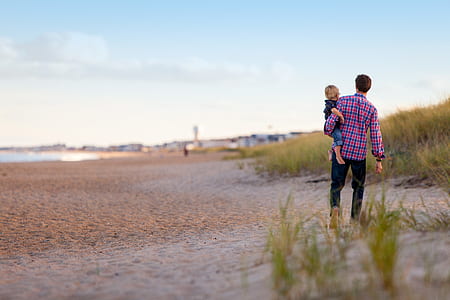man carries boy walks on seashore at daytime thumbnail