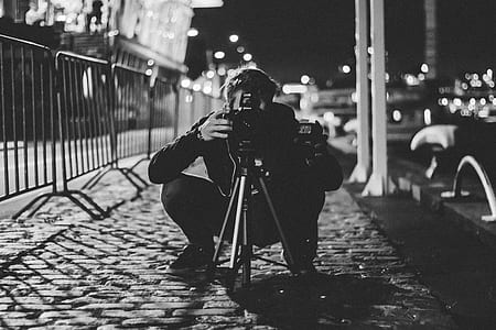 grayscale photography of man taking photo using DSLR camera at nighttime thumbnail