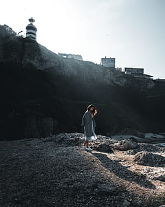 woman holding gray jacket standing on sand thumbnail