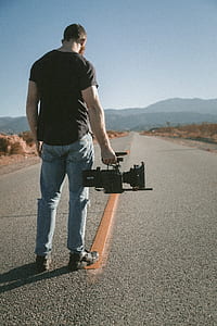man holding video camera standing on road during daytime thumbnail