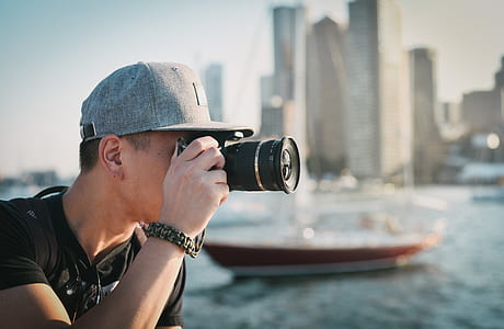 man wearing gray flat brim cap while using black DSLR camera during daytime thumbnail