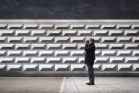man taking a photo beside grey wall during daytime thumbnail
