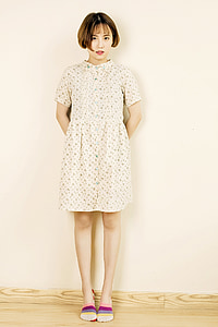 woman in gray and green floral dress leaning on white painted wall thumbnail