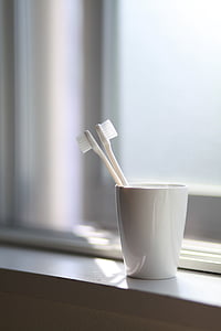 two white toothbrush on white ceramic mug near wall thumbnail