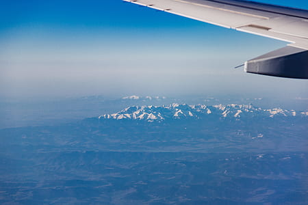 airplane above mountain under white clouds and blue sky thumbnail